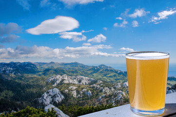 Glass of light wheat beer against mountains background. View of green valley in the mountains.