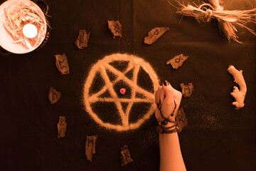 brujería, oráculo o lectura con runas de madera, estrella pentagonal de arena con manos de mujer sobre fondo negro, velas y amuletos