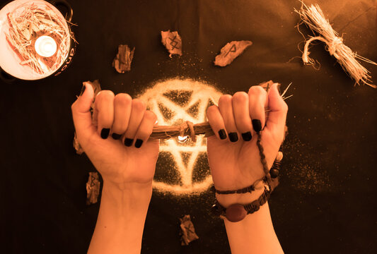brujería, oráculo o lectura con runas de madera, estrella pentagonal de arena con manos de mujer sobre fondo negro, velas y amuletos