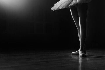 Ballet dancer's legs in pointe shoes on theater stage. Ballerina standing in 3 third position on black and white background. Beautiful woman's feet. Lady shows classic pas. Copy space.