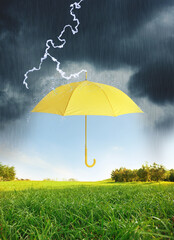 Open yellow umbrella under heavy rain in green meadow