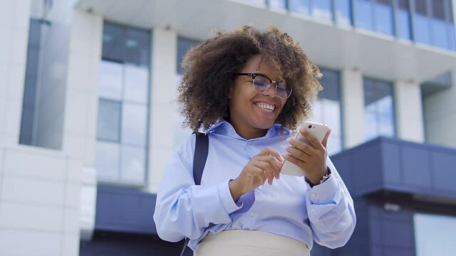 Happy afro-american female reading good news message on smartphone, dancing and smiling. Excited female company employee celebrating promotion, successful career. Making investment in mobile app