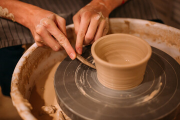 Men's hands are large, they decorate a mug of clay on a pottery table with a knife. Removes excess pieces of clay with a stack