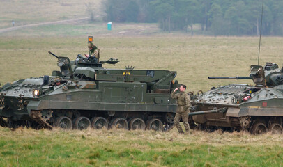 Fototapeta premium with faces obfuscated army mechanized recovery vehicle preparing to tow a stricken infantry fighting vehicle tank on a military exercise Wiltshire UK