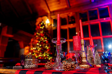 Cozy living room with Christmas decorations at the table. Christmas decorated room with many lights, candles and red light. Room with armchairs and carpet