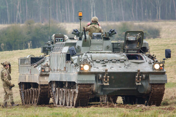 with faces obfuscated army mechanized recovery vehicle preparing to tow a stricken infantry fighting vehicle tank on a military exercise Wiltshire UK