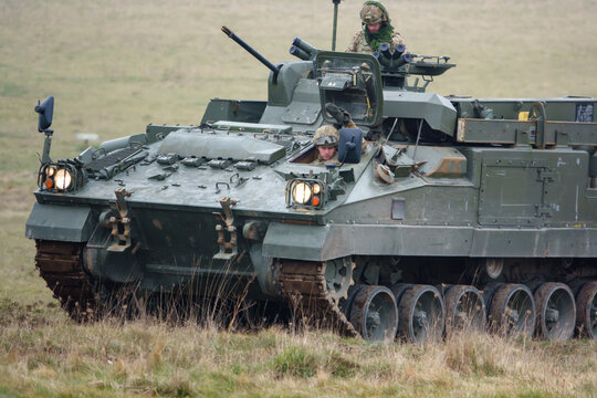 with faces obfuscated army mechanized recovery vehicle preparing to tow a stricken infantry fighting vehicle tank on a military exercise Wiltshire UK