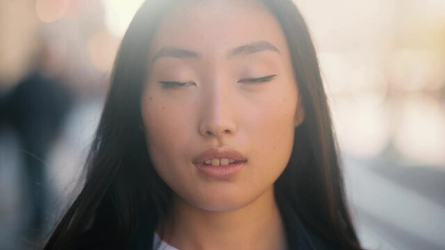 Portrait of young beautiful asian woman walking down and looking at the camera at the sunset. Close up of happy young girl smiling. High quality 4k footage