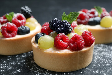 Delicious tartlets with berries on black table, closeup