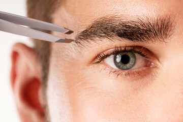 Male eye and tweezers for eyebrow grooming and shape correction