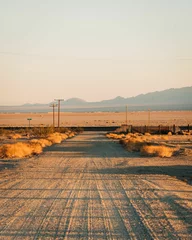 Poster Dirt street with mountains in the distance in Amboy, on Route 66 in the Mojave Desert of California © jonbilous