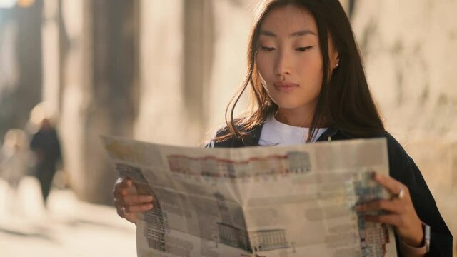 Asian lady walking down the street, looking for way using paper map in old town. Attractive young tourist getting lost in big city trying to find route. High quality 4k footage