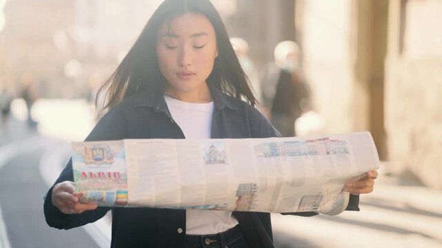 Asian lady walking down the street, looking for way using paper map in old town. Attractive young tourist getting lost in big city trying to find route. High quality 4k footage