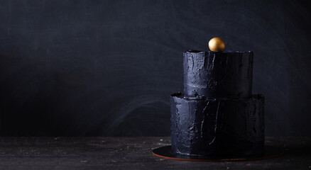 Black bunk cake on the dark black background with golden stars and spheres decoration on top....