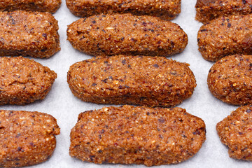 Handmade carbohydrate protein sports bars on white baking paper, close-up. Consist of: peanuts, dates, sesame seeds, prunes, pumpkin seeds, sunflower seeds, oatmeal, dried apricots, almonds, walnuts.