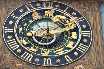 Fototapeta na wymiar antique city hall clock on painted wall of city hall, golden arrow and dragon as clock hands on blue clock face, golden Roman numerals on outer ring and golden zodiac signs in inner ring