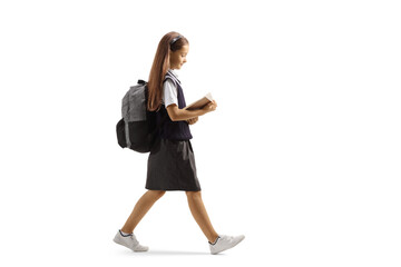 Full length profile shot of a schoolgirl walking and reading a book