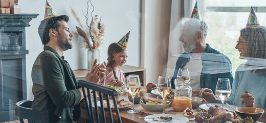 Happy family celebrating birthday of little girl while sitting at the dining table at home