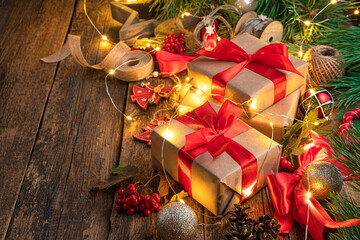 Christmas gifts, toys and pine branches in the light of a garland on a wooden background. Side view, copy space.