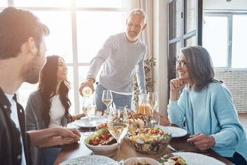 Happy senior man poring wine and smiling while having dinner with family