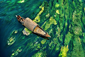 People guide their boats through tranquil, water color-like green reeds and algae on the Karatoya...