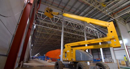 In a workshop under construction, car lifts raise workers in their cradle to the ceiling to perform work there
