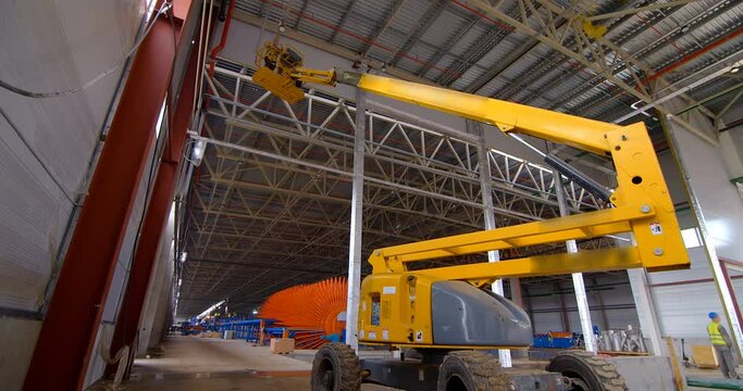 In a workshop under construction, car lifts raise workers in their cradle to the ceiling to perform work there