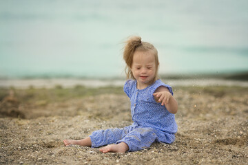 beautiful girl with Down syndrome throwing sand on the seashore