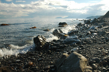 Fototapeta na wymiar Waves breaking onto a stony seashore. Seascape. Foamy waves rush onto the rocky shore. Cloudy.