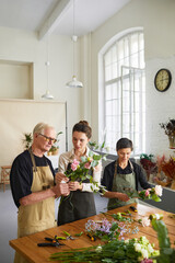 Vertical portrait of young female florist teaching mature couple arranging flower compositions in...