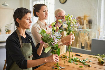Side view portrait of three florists arraigning flower compositions in cozy workshop, copy space