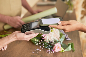 Side view close up of female customer paying via smartphone in flower shop, copy space