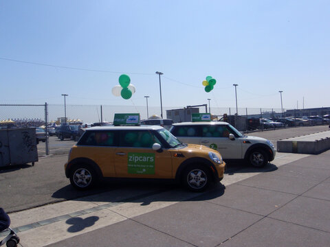 Two ZipCars Mini Coopers filled with balloons parked on sidewalk