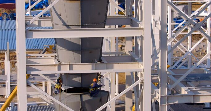 At the construction site where a new, modern plant is being built, worker assemblers at a height assemble industrial equipment 