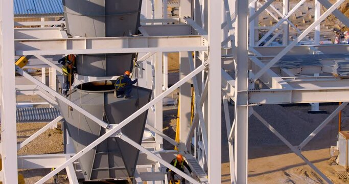 At the construction site where a new, modern plant is being built, worker assemblers at a height assemble industrial equipment 