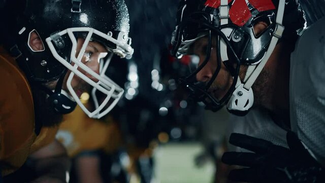 American Football Game Start Teams Ready: Close-up Portrait of Two Professional Players, Aggressive Face-off. Competition Full of Brutal Energy, Power, Skill. Cinematic Rainy Night. Dramatic Light
