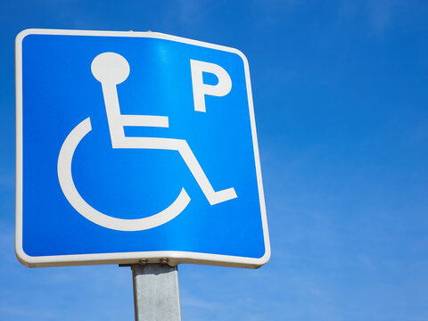 Detail of a vertical pole sign marking a parking for disabled people vehicles against the blue sky background as a copy space.