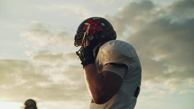 American Football Championship Game: Close-up Portrait of Professional White Player, Putting on Helmet, Looking at Camera. Professional Athlete Determined to Win. Cinematic Low Angle Shot