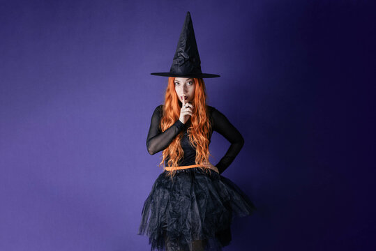 Young witch halloween costume purple wall background showing silence gesure