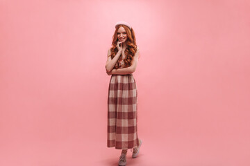 Slender young caucasian lady stands in full growth on pink background, smiling broadly. Girl with...