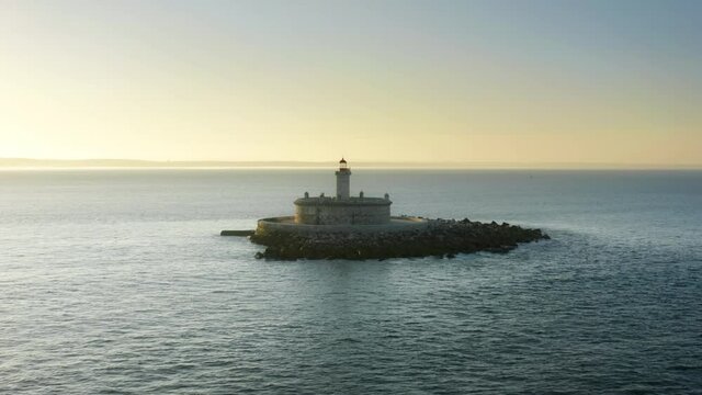Lisbon. Portugal. A prominent landmark of the Forte do Bugio lighthouse set offshore. Drone footage of picturesque coast under sunset sky. High quality 4k footage