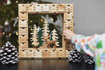A girl opens wooden advent calendar with presents - obrazy, fototapety, plakaty
