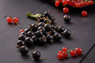 black currant berries lie on a black wooden surface. Next to the red currant berries. Close-up.