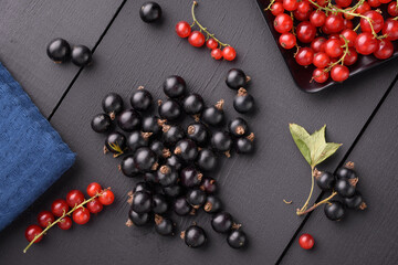 black currant berries lie on a black wooden surface. Next to it is a blue napkin and red currant berries.