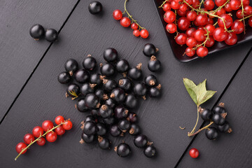 black currant berries lie on a black wooden surface. Next to the red currant berries.