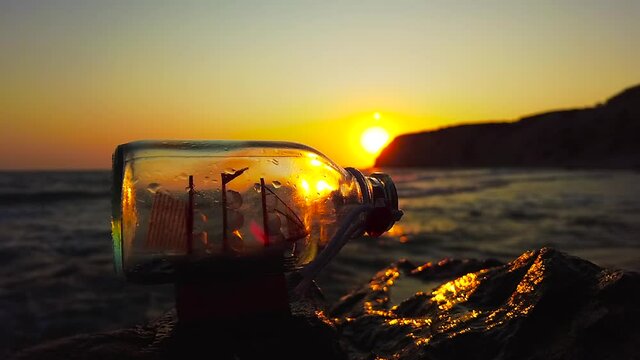 A ship in a bottle stands on a rock in front of the sea at sunset, Kos, Greece