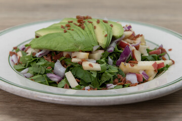 Spinach salad topped with avocado over chopped vegetables for a healthy portion to your meal plan