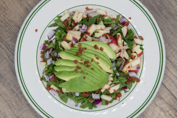 Overhead view of spinach salad topped with avocado over chopped vegetables for a healthy portion to your meal plan