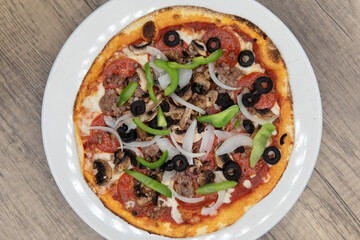 Overhead view of personal sized pizza with equal meat and vegetable toppings of olives, peperoni, sausage, and onions with a crispy crust