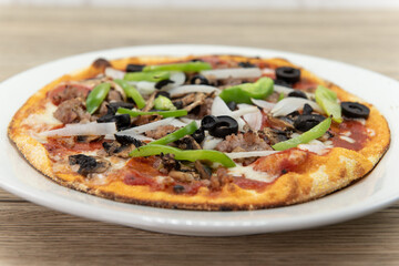 Personal sized pizza chopped vegetables and multiple meat and plenty of toppings with a crispy crust
